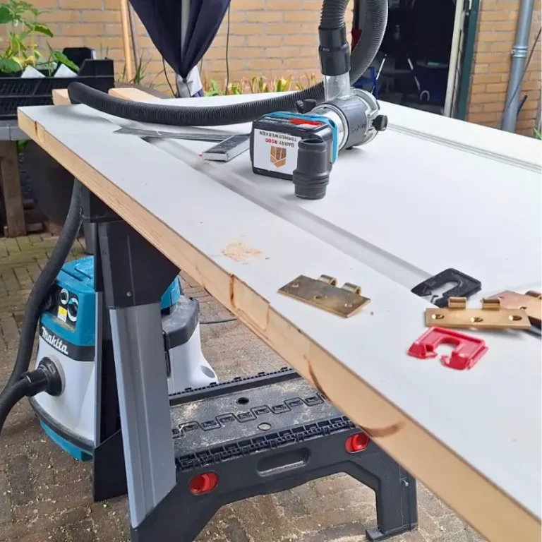 Een witte deur ligt op zaagbokken met gereedschap, voorbereid om te worden afgehangen.
