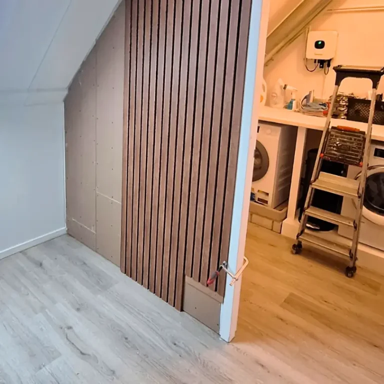 Een gedeeltelijk afgewerkte scheidingswand op een zolder, met gipsplaten aan de ene zijde en een houten lattenwand aan de andere zijde.